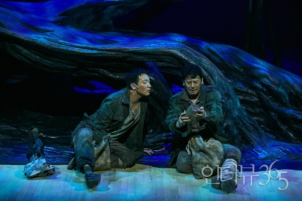 2023 연극 '나무 위의 군대' 공연 사진. 굶주림에 정신을 잃더라도 적군의 식량에 손을 댈 수 없다던 '상관(이도엽)'은 어느 새 적군이 버린 물건들 가운데 기호식품을 챙기는 변화를 보일 뿐 아니라 '신병(손석구)'에게 자본주의의 법칙을 설명한다.