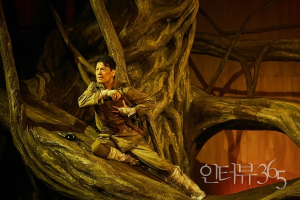 2023 연극 '나무 위의 군대' 공연 사진. '상관(이도엽)'은 제국의 군인인 자신이 목숨을 부지하기 위해 나무로 숨어들었다는 수치심을 들키고 싶지 않기 때문에 신병에게 전략적으로 나무 위에서 잠복을 하는 것이라고 주장한다.