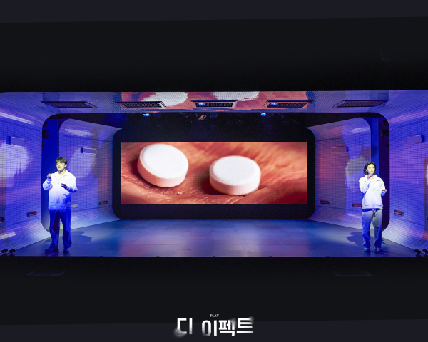 연극 '디 이펙트' 공연 사진. 임상시험 참가자들이 약을 복용하는 행위는 음향을 통한 청각적 효과와 영상을 통한 시각적 효과로 강조된다.