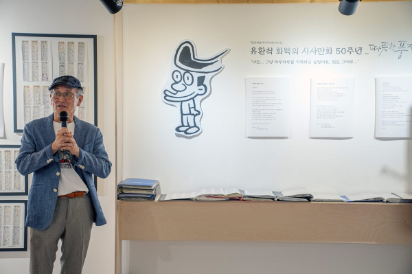 ① 유환석 화백의 대표 캐릭터 《헹가래》가 커다란 하트를 품고 흥겹게 뛰는 모습. 날카로운 현실 풍자 속에서도 사람에 대한 애정과 따뜻한 웃음을 놓지 않은 작품의 성격을 보여준다.② 익살스러운 표정과 경쾌한 몸짓이 돋보이는 《헹가래》 캐릭터. 유 화백과 함께 17년 동안 약 5,000번의 세상을 만나며 스포츠조선을 대표하는 시사만화 캐릭터로 성장했다.③ 유환석 화백이 춘천예술마당 아트프라자갤러리에서 열린 데뷔 50주년 특별전 《따뜻한 풍자》에서 작품 세계를 설명하고 있다. 그의 곁에는 반세기 창작 여정을 함께한 대표 캐릭터 《헹가래》가 자리하고 있다.④ 주가 급등과 롤러코스터 같은 금융시장, 부동산 정책과 중동 정세 등을 다룬 유환석 화백의 《헹가래》. 복잡한 경제·국제 문제를 익살스러운 캐릭터와 간결한 비유로 풀어낸 최근 시사만평이다.
